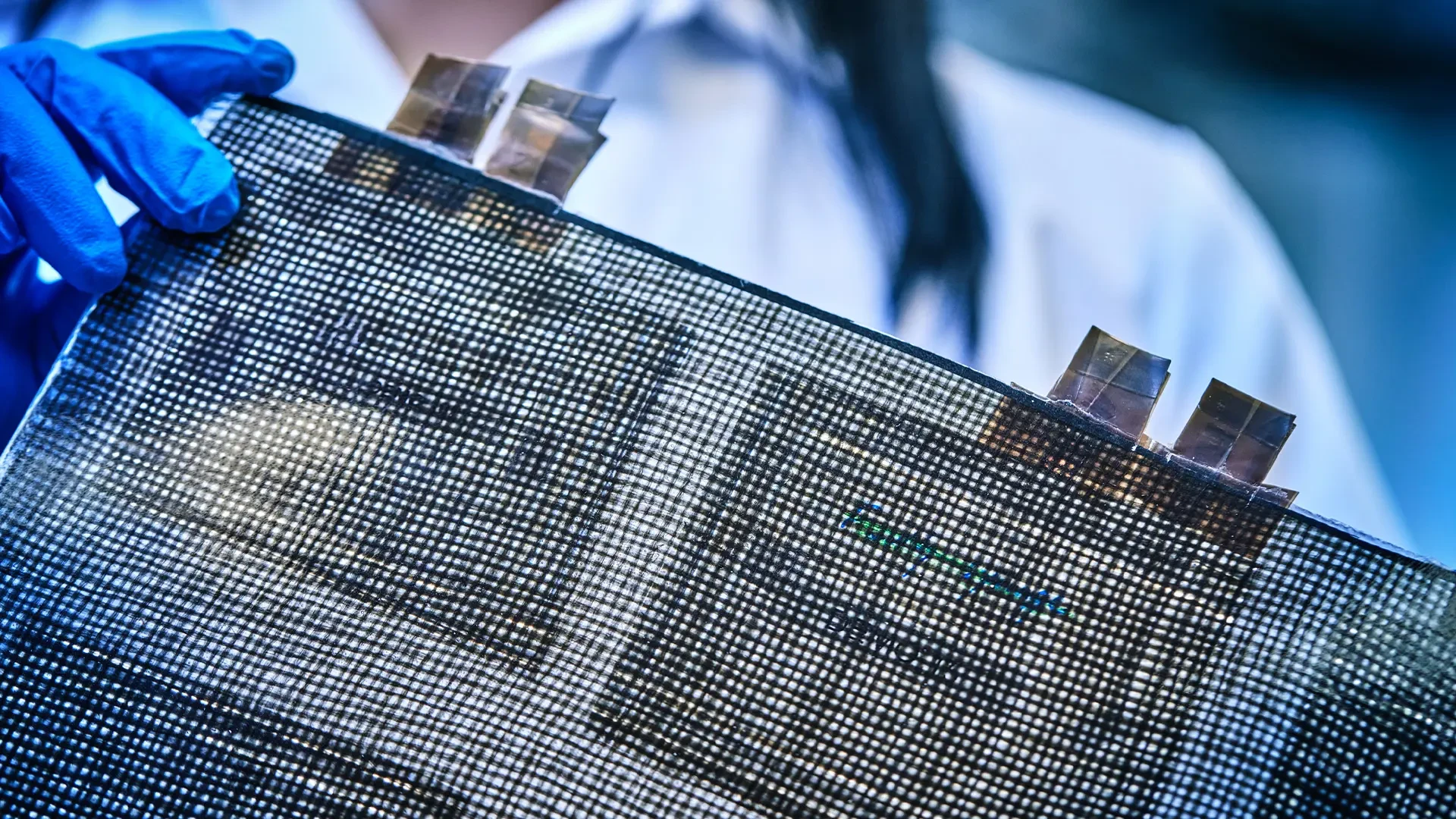Close-up of a structural battery made from carbon fiber composite material, featuring visible conductive tabs and woven texture