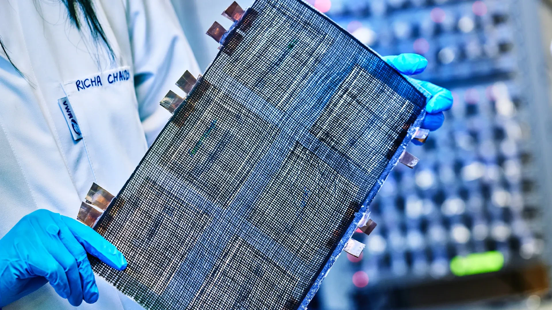 Researcher holding a structural battery prototype made from carbon fiber composite with visible metallic terminals