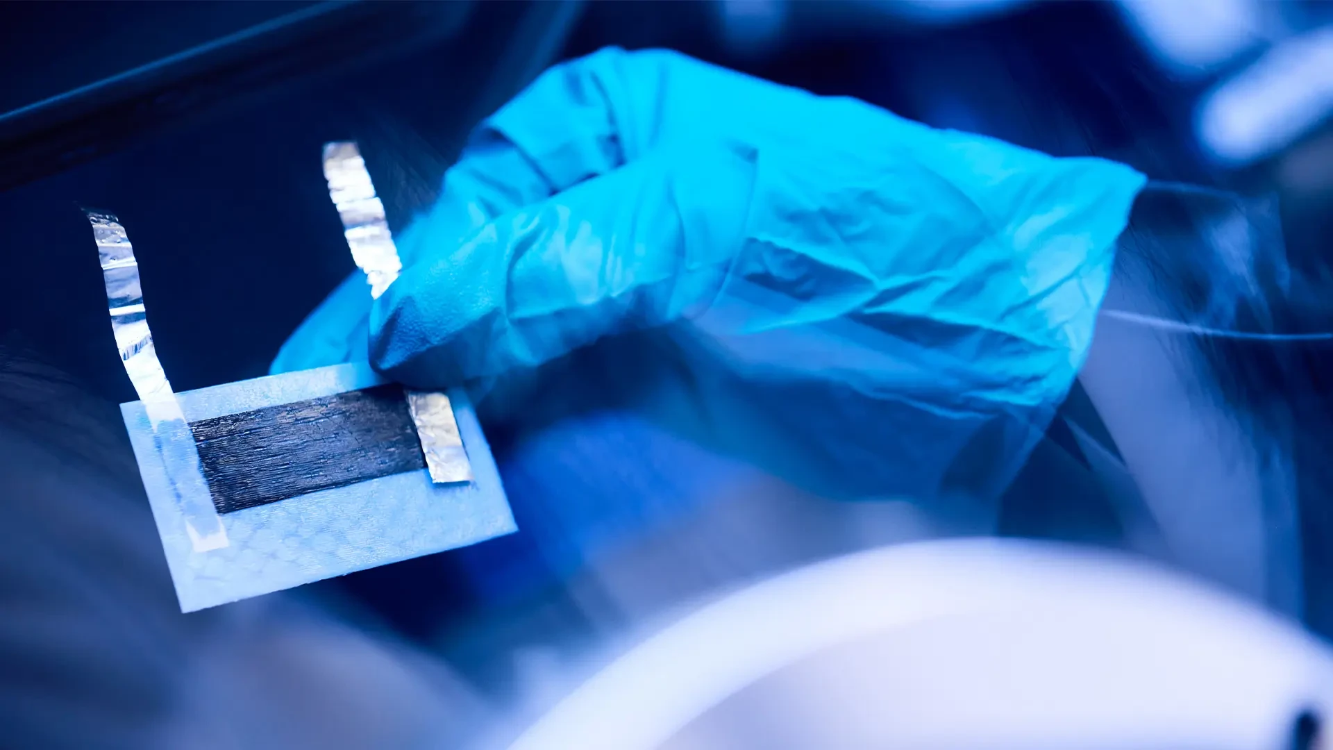Close-up of a structural battery cell made from carbon fiber composite held by a gloved researcher in a Swedish laboratory