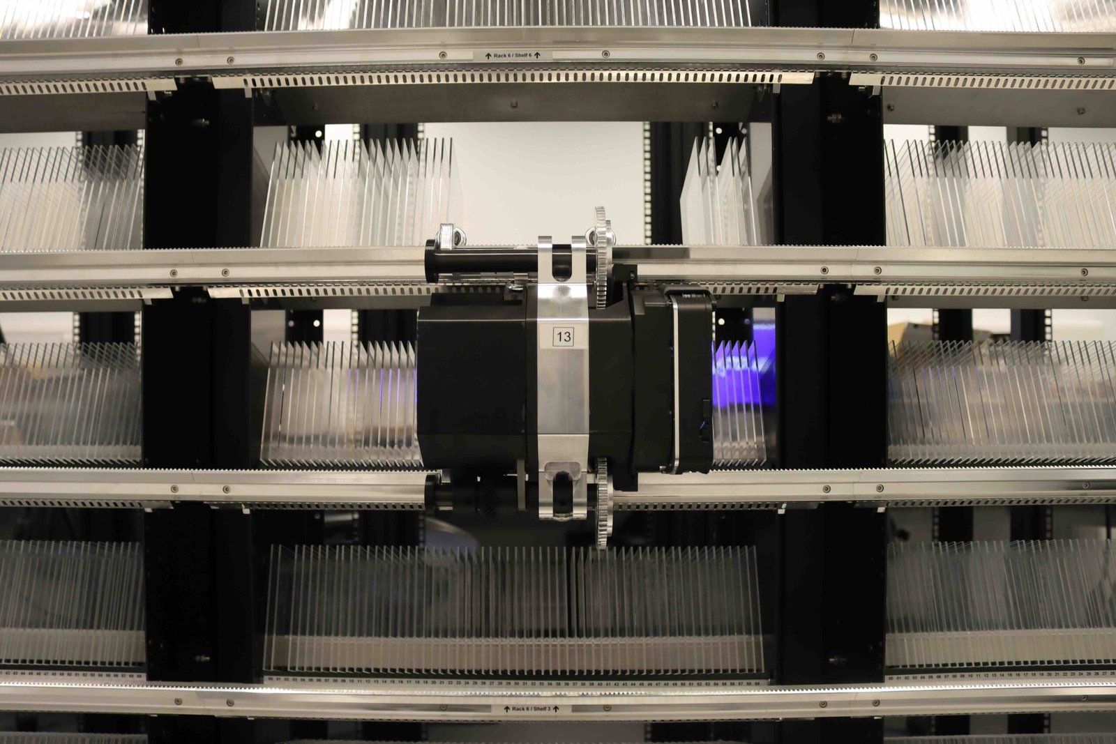 Front view of Microsoft Project Silica’s robotic retrieval unit operating among racks filled with quartz glass data storage plates.