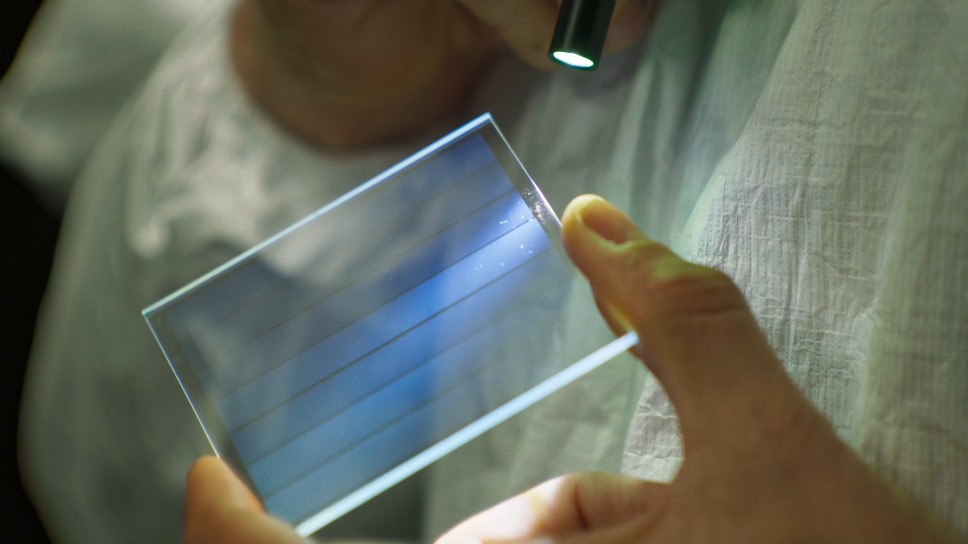 Close-up of a person examining a Microsoft Project Silica quartz glass plate under light, showcasing long-term data storage technology.