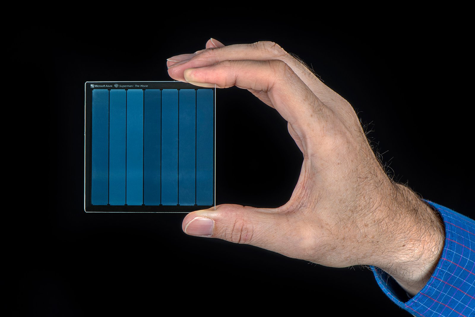 A hand holding a Microsoft Project Silica quartz glass plate, used to store the 1978 Superman movie, demonstrating 7TB archival data storage.